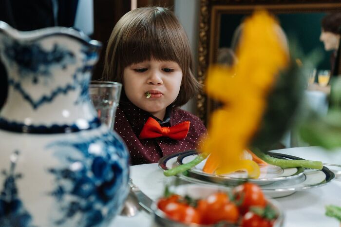 Child with a red bow tie trying vegetables at a family meal, illustrating practical parenting tips and tricks shared by parents.