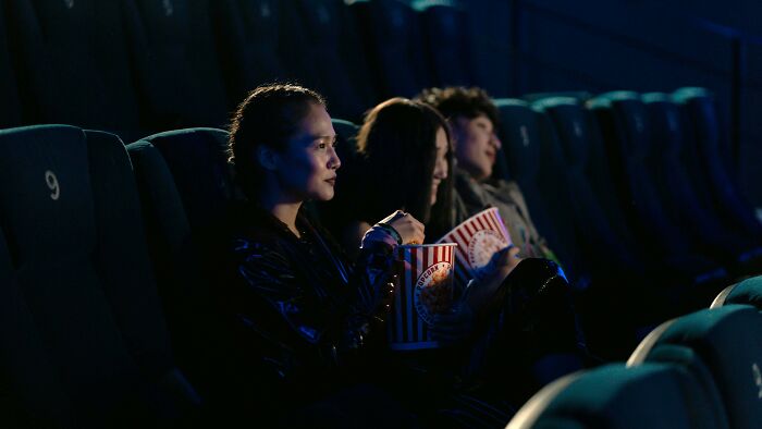 Three people sitting in a dark movie theater holding popcorn, watching a film, illustrating movie knowledge quiz fans.