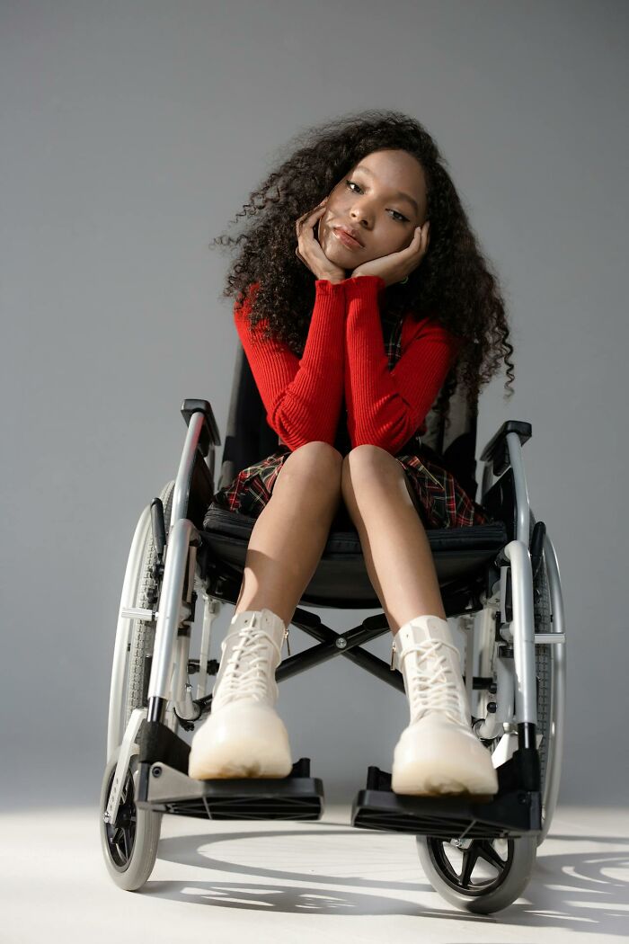 Young woman in wheelchair wearing white boots and red sweater, reflecting on terrifying statistics that impact life challenges.
