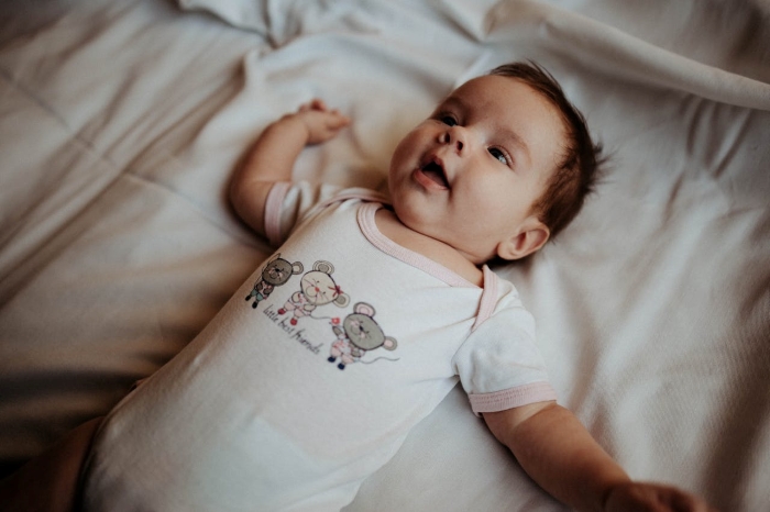 Baby lying on a bed in a white onesie, illustrating concerns about mom&rsquo;s creepy behavior and psychotic tendencies.