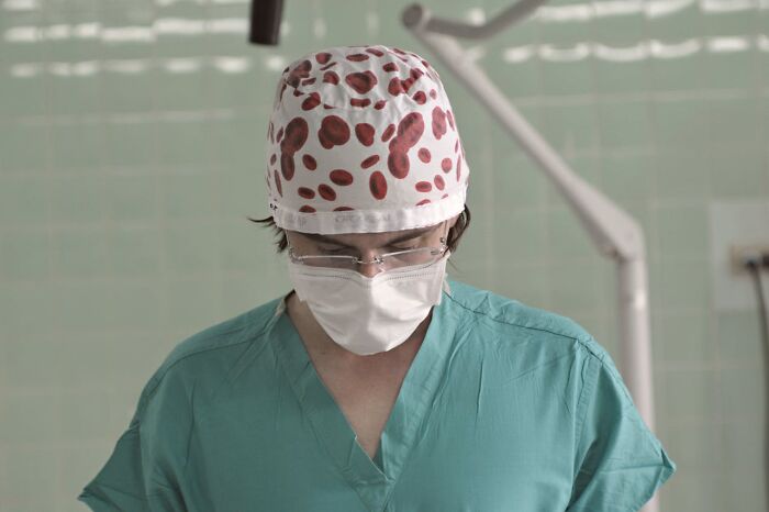 Gynecologist in surgical scrubs and mask focused on a procedure in a clinical medical setting.