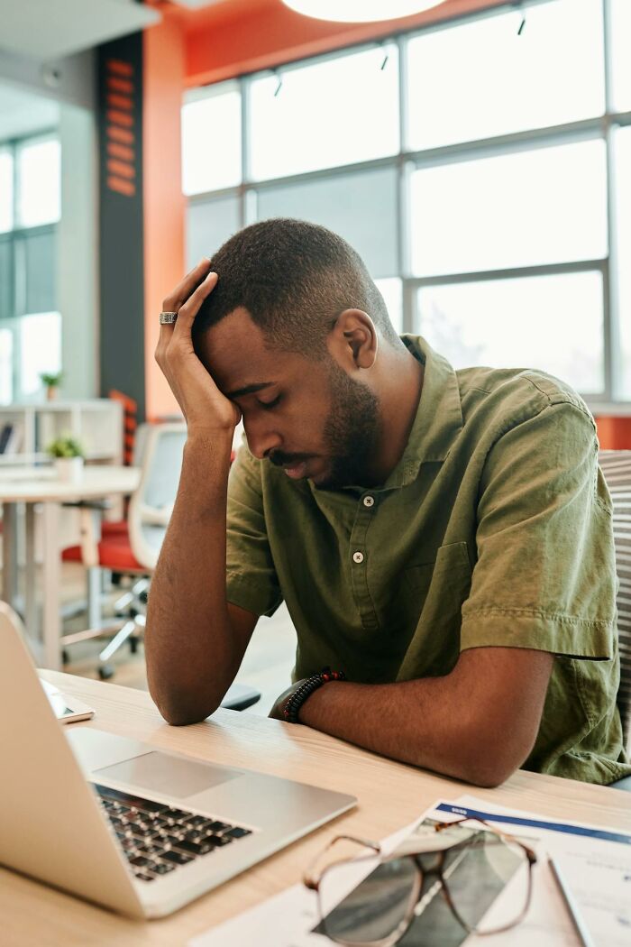 Stressed employee sitting at desk with laptop, showing frustration in a modern office workspace environment.