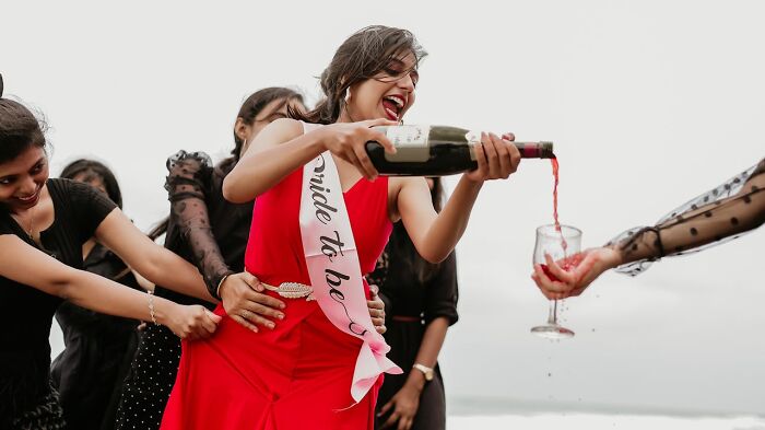 Bride to be in red dress pouring wine at a lively bachelor and bachelorette party with friends enjoying the celebration outdoors