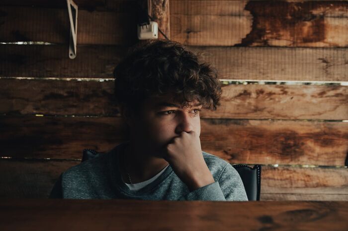 Teen boy sitting indoors looking thoughtfully to the side, representing stories about life dealing with horrible bullies.