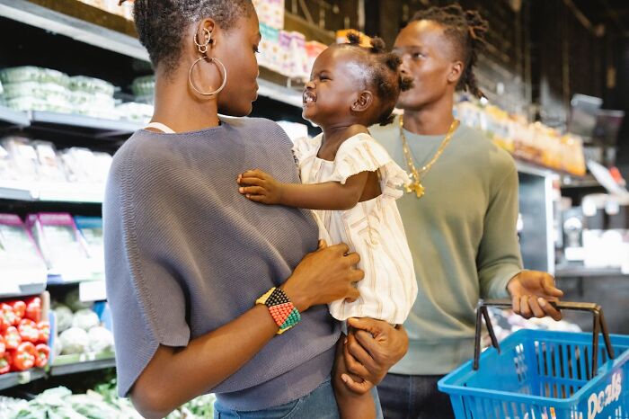Parent holding smiling child with father shopping in grocery store using tips and tricks parents share.