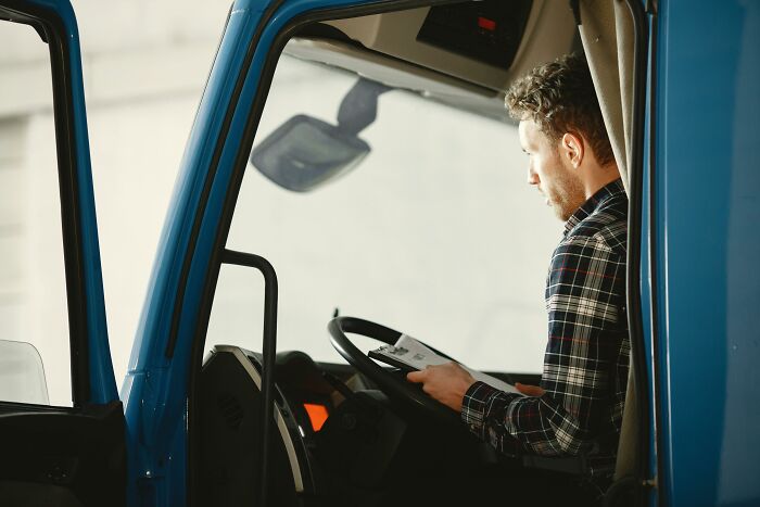 Man in a plaid shirt sitting inside a blue truck, looking at a document related to DNA tests and ancestry results.