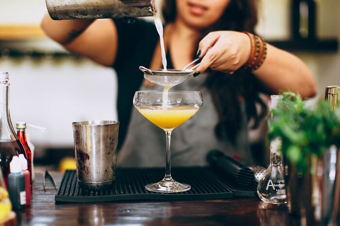Bartender straining a cocktail into a glass, capturing the party drinks often seen at bachelor and bachelorette parties.