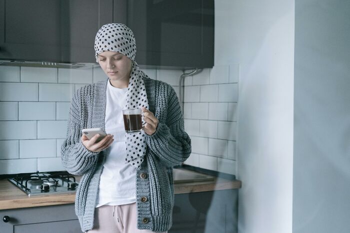 Young woman wearing a headscarf holding a cup of coffee while looking at her phone, depicting friendship struggles and emotions.