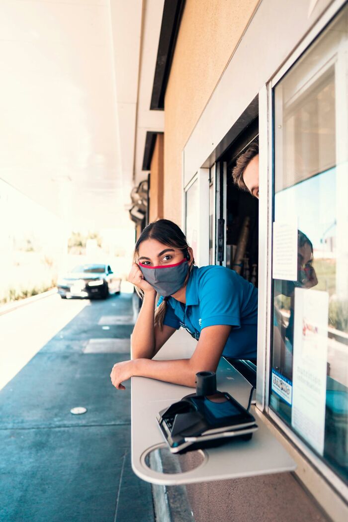 Young woman wearing a mask leaning at a drive-thru window, illustrating stories about moms and everyday moments.