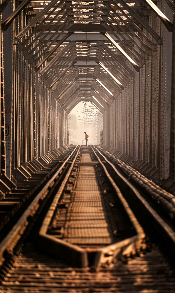 A lone figure stands on railroad tracks inside a long, metal tunnel. A satisfying picture for a gentle reset.