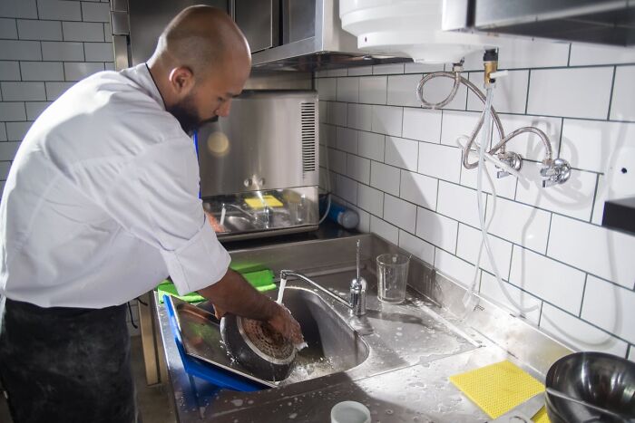 Employee washing dishes in a commercial kitchen during a wild times shift before quitting the job immediately.
