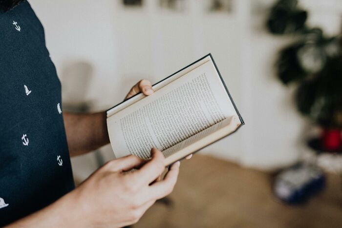 Person holding and reading a book closely, testing spelling mistakes and attention to detail in a quiet indoor setting.