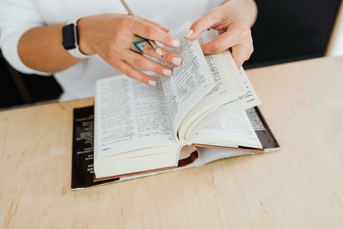 Person wearing a watch and ring flipping through pages of a dictionary for advanced English words learning.