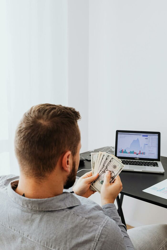 Man holding cash while analyzing financial charts on a laptop, illustrating terrifying statistics about money and sleep.