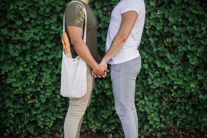 Two men holding hands in front of an ivy wall, one carrying baguettes, representing those who leave the church.