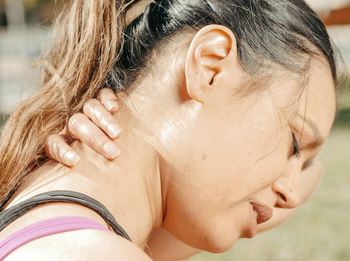 Woman outdoors holding her neck in pain, highlighting concerns about buffalo hump and potential health issues. Woman outdoors holding her neck in pain, highlighting concerns about buffalo hump and potential health issues.