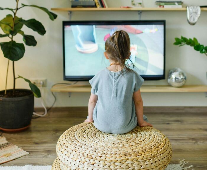 Child sitting on a woven stool watching TV in a cozy living room, illustrating tips and tricks parents share.