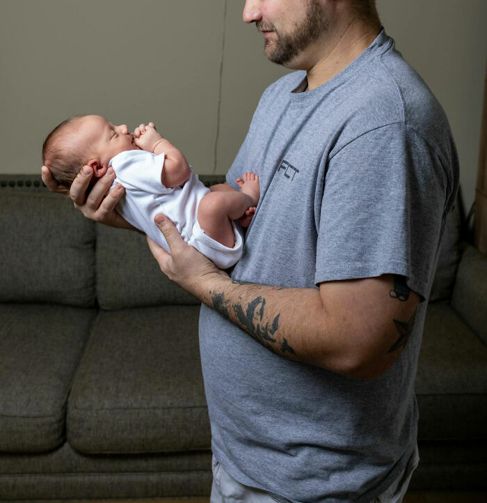 Man with tattoos holding a newborn baby gently, capturing a moment of emotional intuition and connection at home.