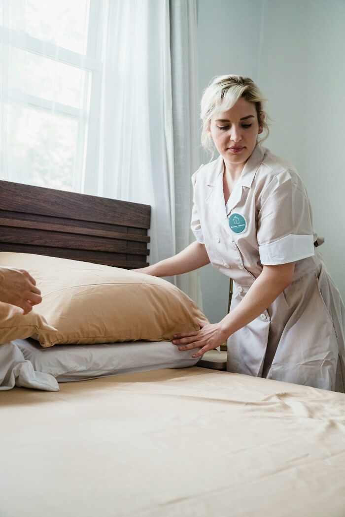 A blonde woman in a maid uniform makes a bed, symbolizing the unseen effort in many workplace incidents.