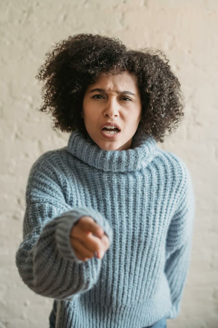 Angry employee in a blue sweater pointing forward expressing frustration about quitting job immediately at work.