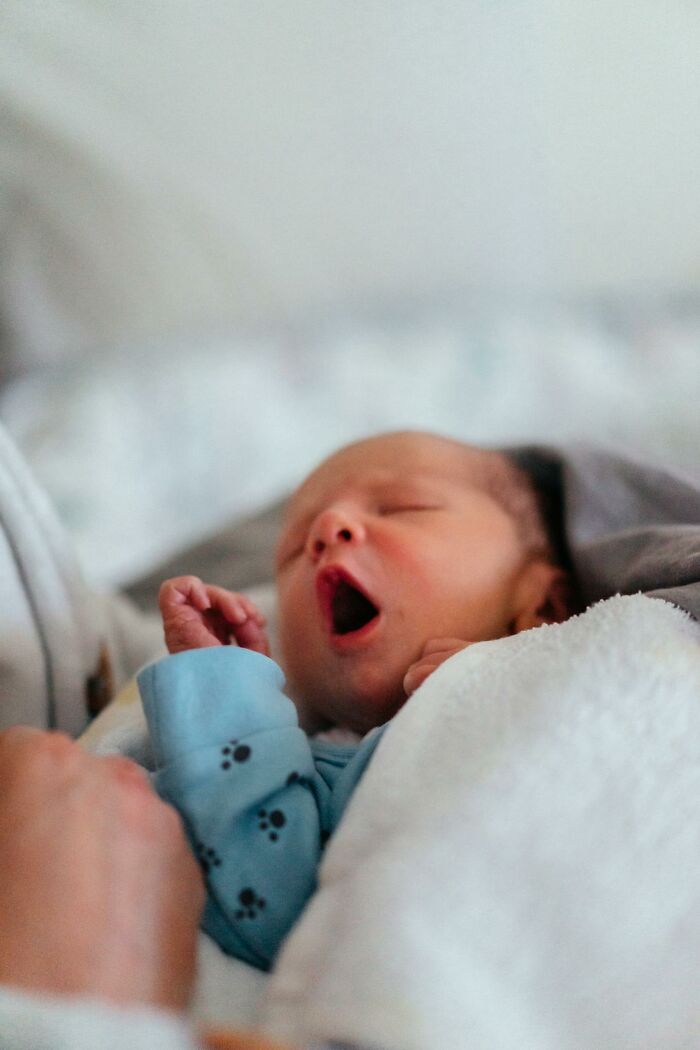 Newborn baby yawning and wrapped in a white blanket, illustrating weird and interesting medical facts about infants.