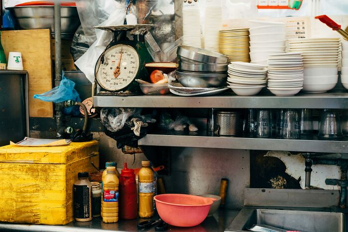 A cluttered, busy kitchen counter with an old scale, stacks of dishes, and bottles. Workplace incidents can arise from such environments.