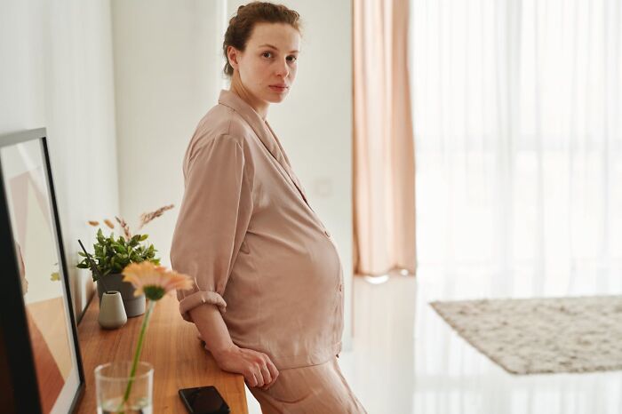 Pregnant woman in neutral pajamas looking tired and concerned, illustrating terrifying statistics affecting sleep quality.