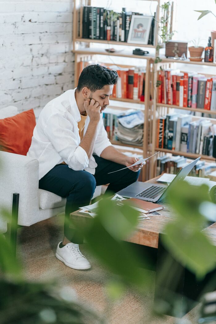 A man intently reads documents at a coffee table with a laptop, reflecting on family secrets.