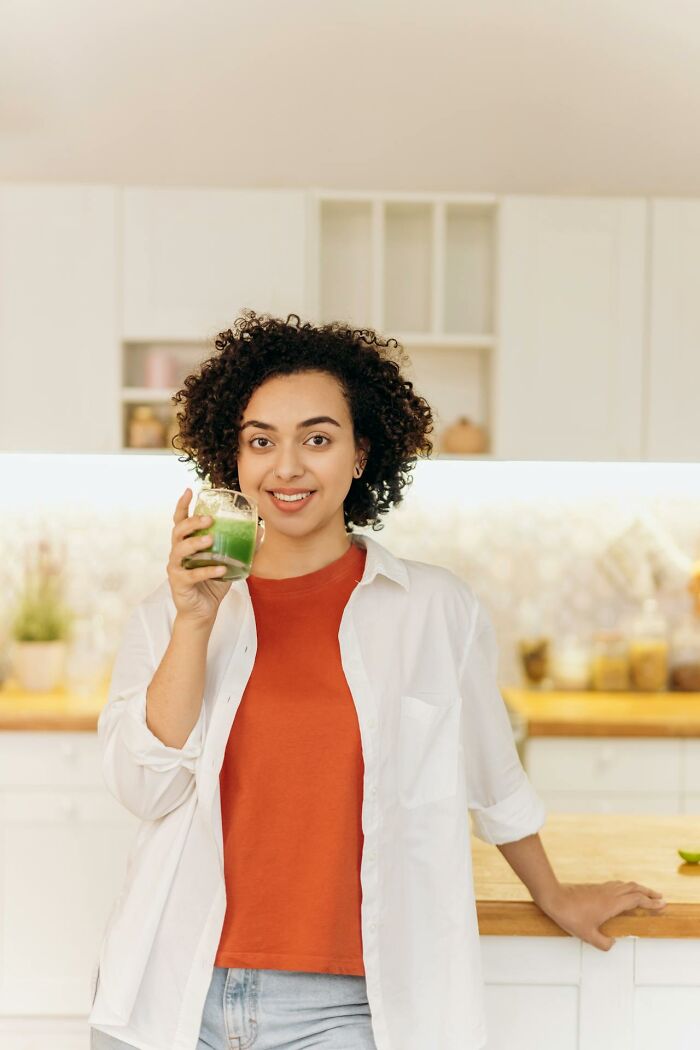 Young woman in casual wear holding a green smoothie in modern kitchen illustrating weird and interesting medical facts