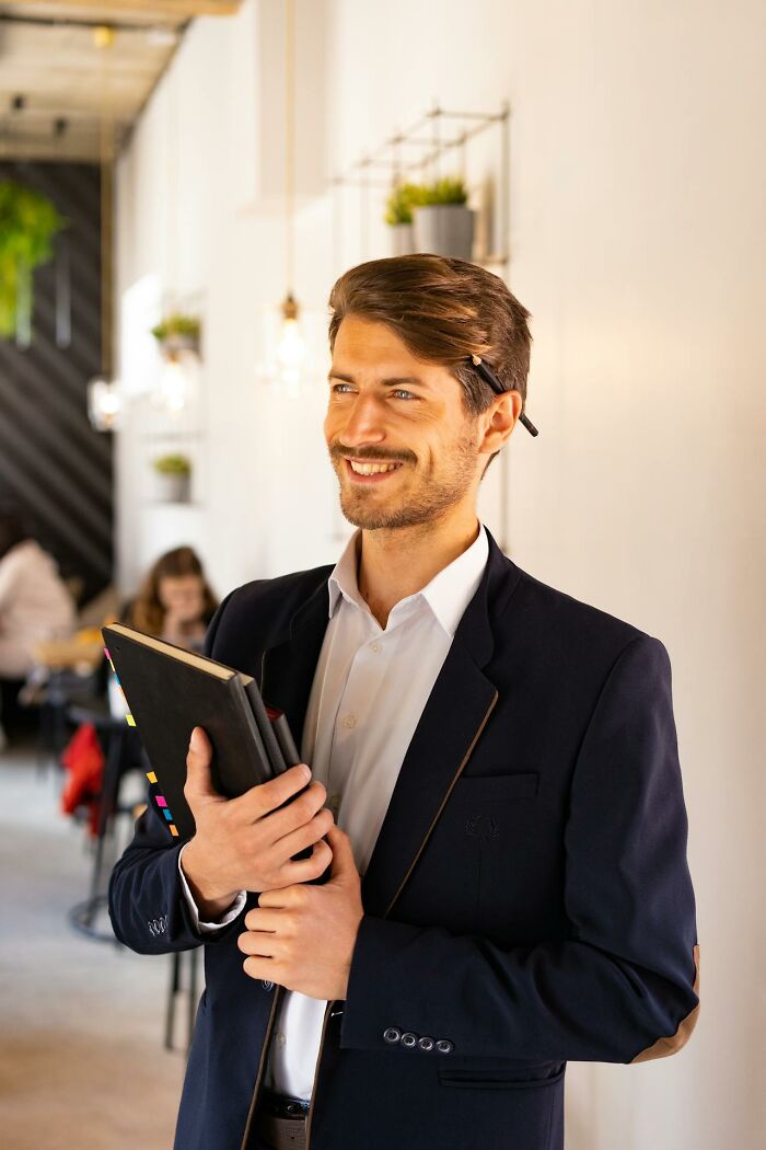 Young professional man holding notebook and smiling in modern office, reflecting wild times employees deciding to quit job.