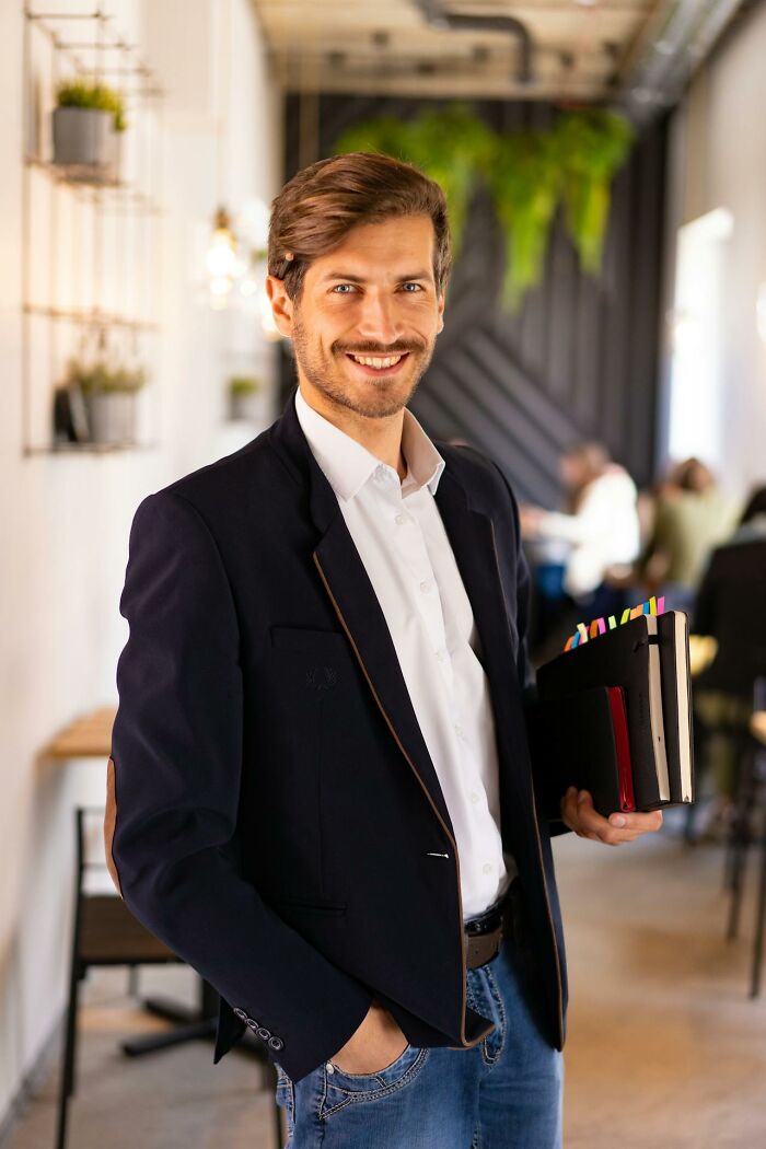 Smiling man in casual blazer holding folders with colorful tabs, representing stories about people seeing their intuition proved right.