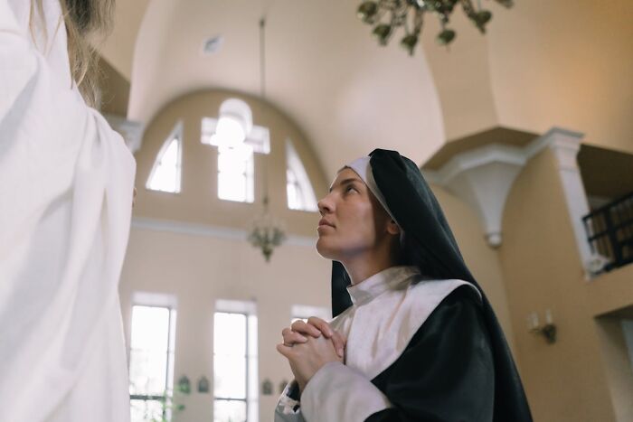 A nun, hands clasped, looks up in a church. She is a former priest or nun who left the church.