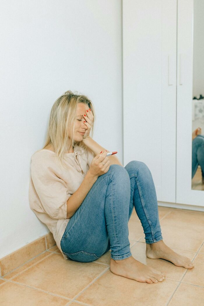 Woman sitting on floor, looking distressed while holding a pregnancy test, reflecting on dark family secrets.