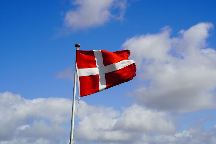 Flag of Denmark waving against a blue sky, part of an 18-question world flag quiz to test recognition skills.