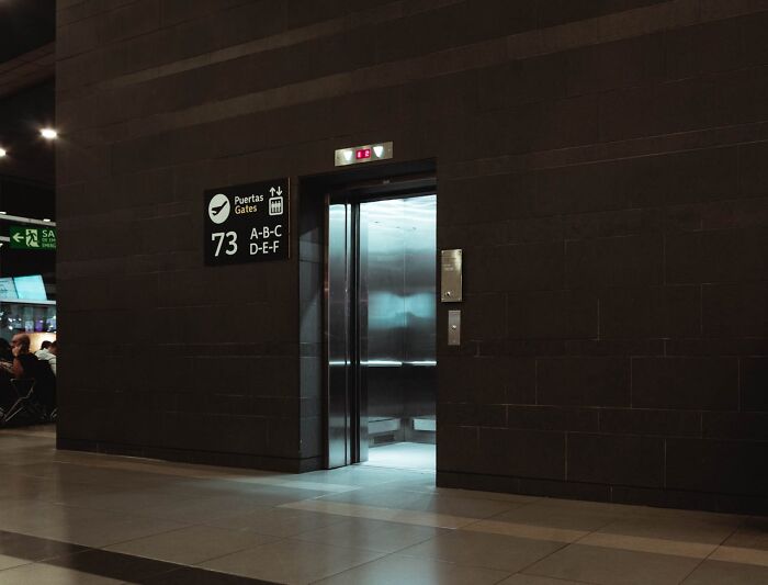 Elevator doors open in a dimly lit airport terminal near gate signs in a scene hinting at unexpected and bizarre incidents.
