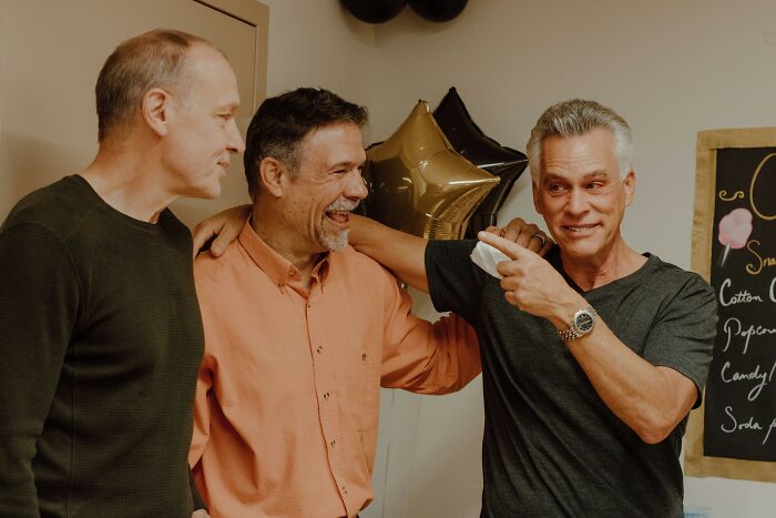 Three men sharing a laugh, one pointing while another has an arm around him. Friends sharing cheat codes for adult life.