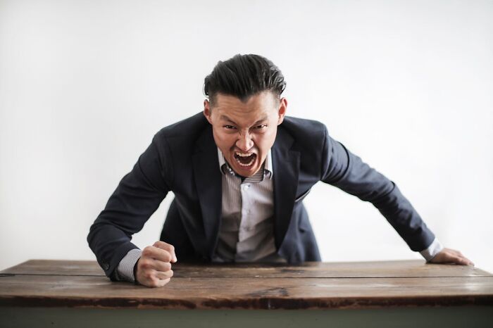 Angry employee in business attire pounding fist on desk expressing frustration at work before quitting job.