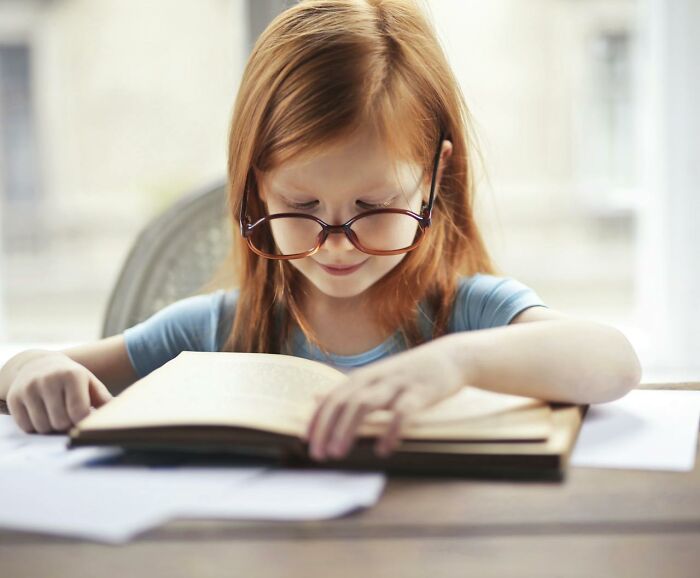 Young girl with glasses reading a book intently, illustrating focus on terrifying statistics that might make it hard to sleep