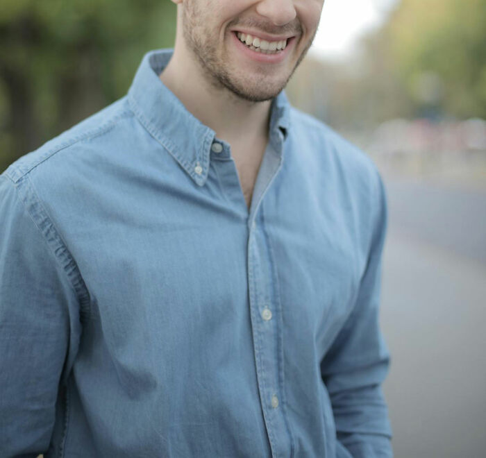 Young man smiling outdoors feeling confident about his intuition being proved right in a casual blue shirt.