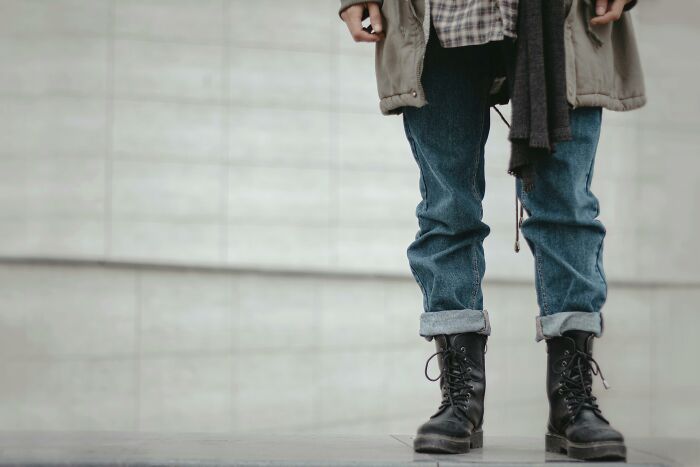 Person wearing urban style boots and jeans standing against a plain wall representing urban legends concept.