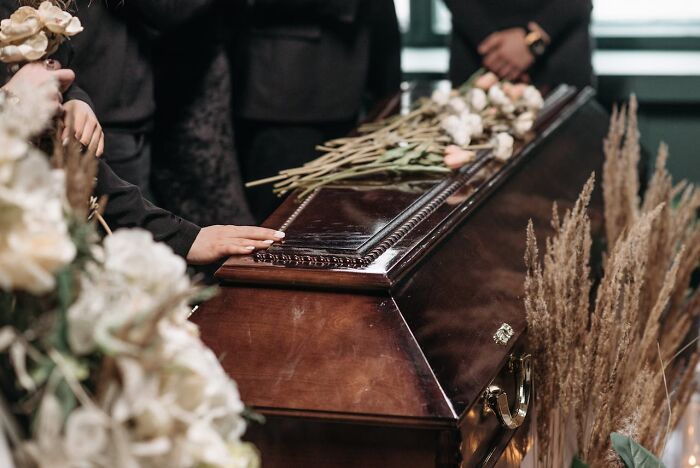 Mourning people gathered around a coffin with flowers, representing unexpected and bizarre ways people passed away.