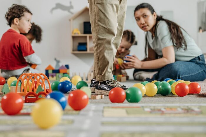 Children playing with colorful balls and toys on the floor while employees watch in a daycare setting
