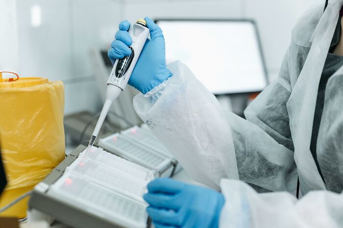 Scientist in protective gear using a pipette for DNA testing in a laboratory, highlighting unexpected heritage results.