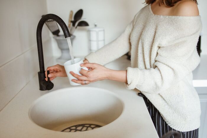 Person filling white cup with tap water in kitchen sink, illustrating terrifying statistics about drinking water safety.