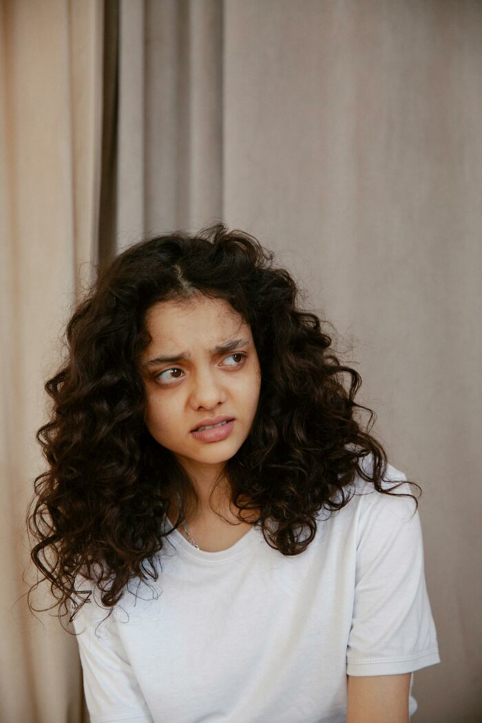 Young woman with curly hair wearing a white shirt looking uneasy, illustrating wild times employees needing to quit work immediately.