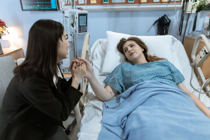 Woman in hospital bed holding hands with her mother, sharing an emotional and touching moment between moms and children.