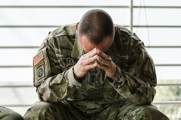 A soldier in uniform sits with his head in his hands, appearing distressed. He is wearing a MAGA patch. A painful divorce can be devastating.