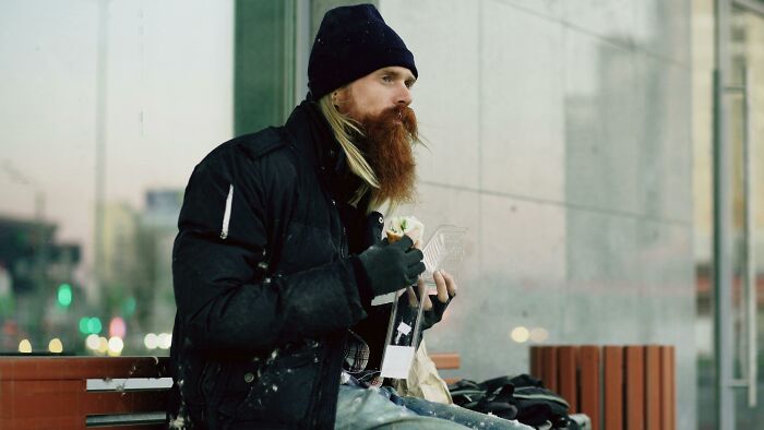 A person with a long beard and beanie eating outdoors. The image invokes feelings of group therapy and messy confessions.