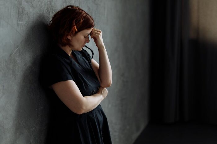 Woman in black dress leaning against a wall, appearing emotional, representing amazing and interesting stories about moms.