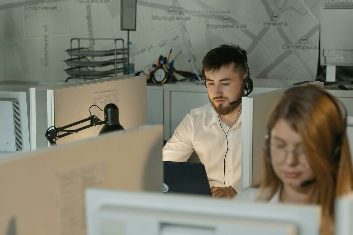 A man wearing a headset and white shirt works on a laptop at a call center. Disturbing sounds might arise from his calls.